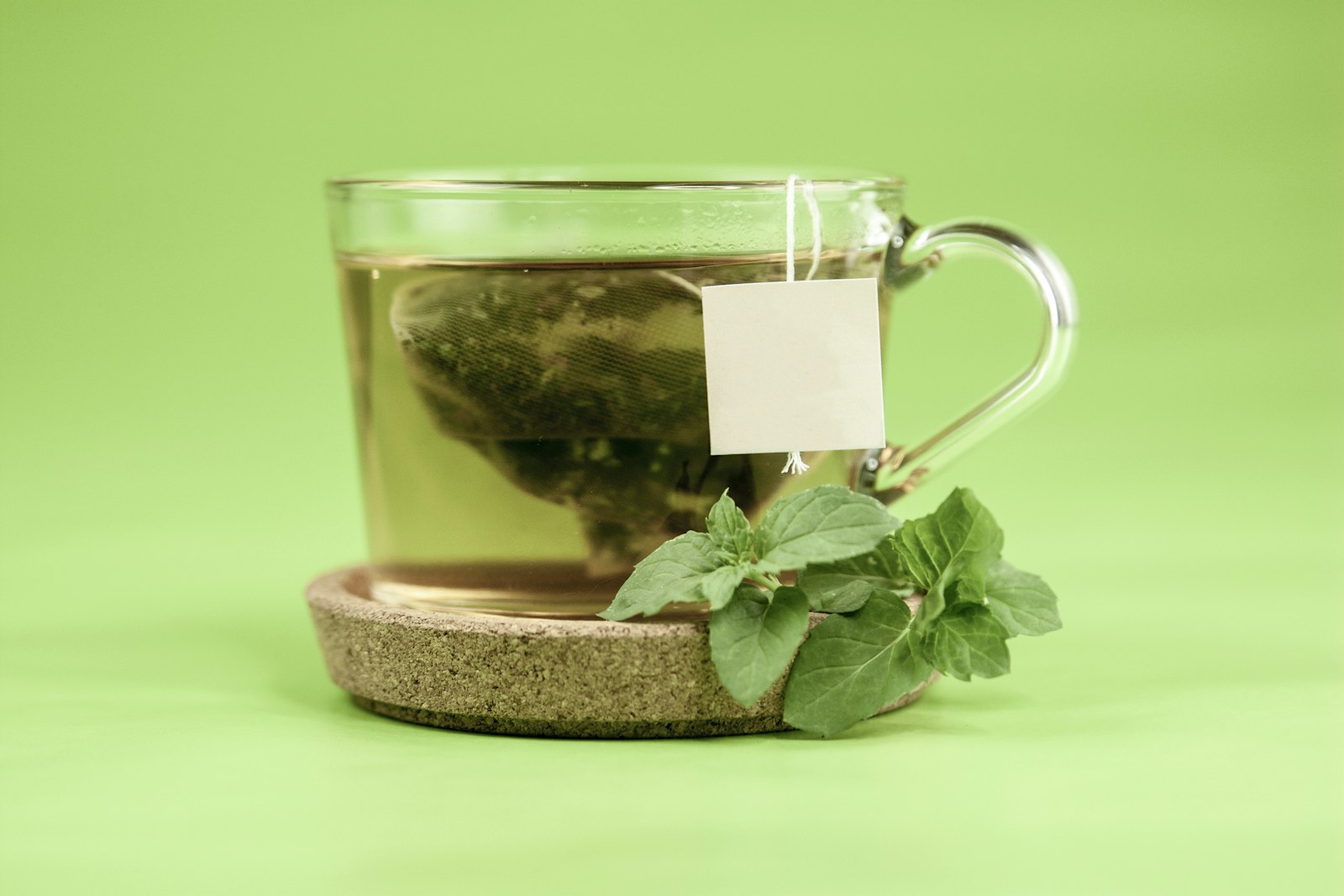 A glass cup of herbal tea beside fresh leaves
